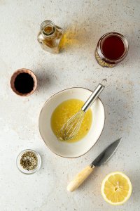 Zubereitung der Marinade: Eine kleine Schüssel mit Zitronensaft und fein gewürfeltem Knoblauch, daneben eine Schüssel mit getrockneten Kräutern und Salz, Balsamico, Honig und eine Flache Olivenöl