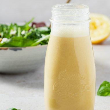 Salatdressing in einer Glasflasche, im Hintergrund eine Salatschüssel und eine halbe Zitrone
