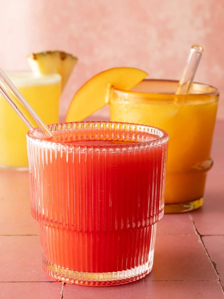 Drei Gläser Agua Fresca in verschiedenen Farben, vorne rote Erdbeer Agua Fresca mit Glasstrohhalm.