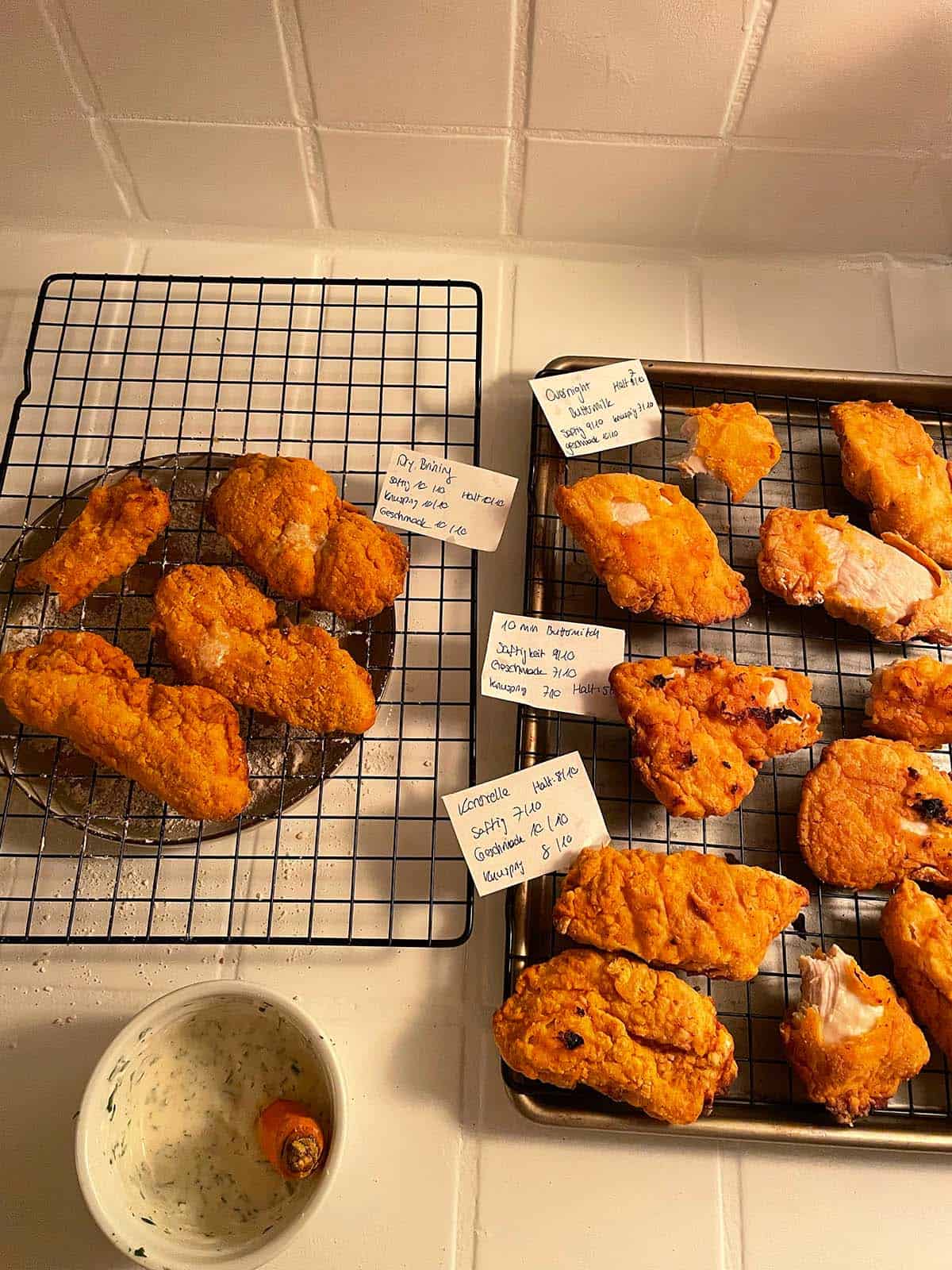 4 verschiedene Testversuche von Fried Chicken im Airfryer auf einer Küchenarbeitsfläche mit jeweiligen Beschriftungskarten.