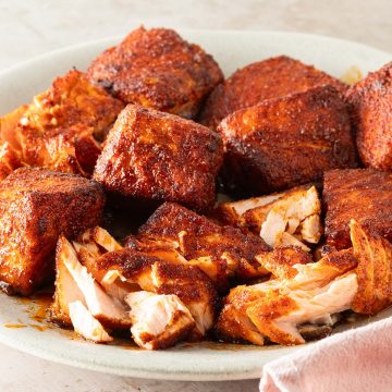 Saftige, w&uuml;rzig marinierte Lachsw&uuml;rfel aus dem Airfryer mit knuspriger Kruste auf einem Teller, teilweise aufgeschnitten, sodass das zarte, saftige Innere sichtbar ist.