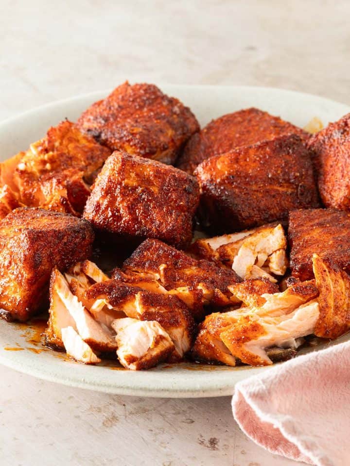 Saftige, w&uuml;rzig marinierte Lachsw&uuml;rfel aus dem Airfryer mit knuspriger Kruste auf einem Teller, teilweise aufgeschnitten, sodass das zarte, saftige Innere sichtbar ist.