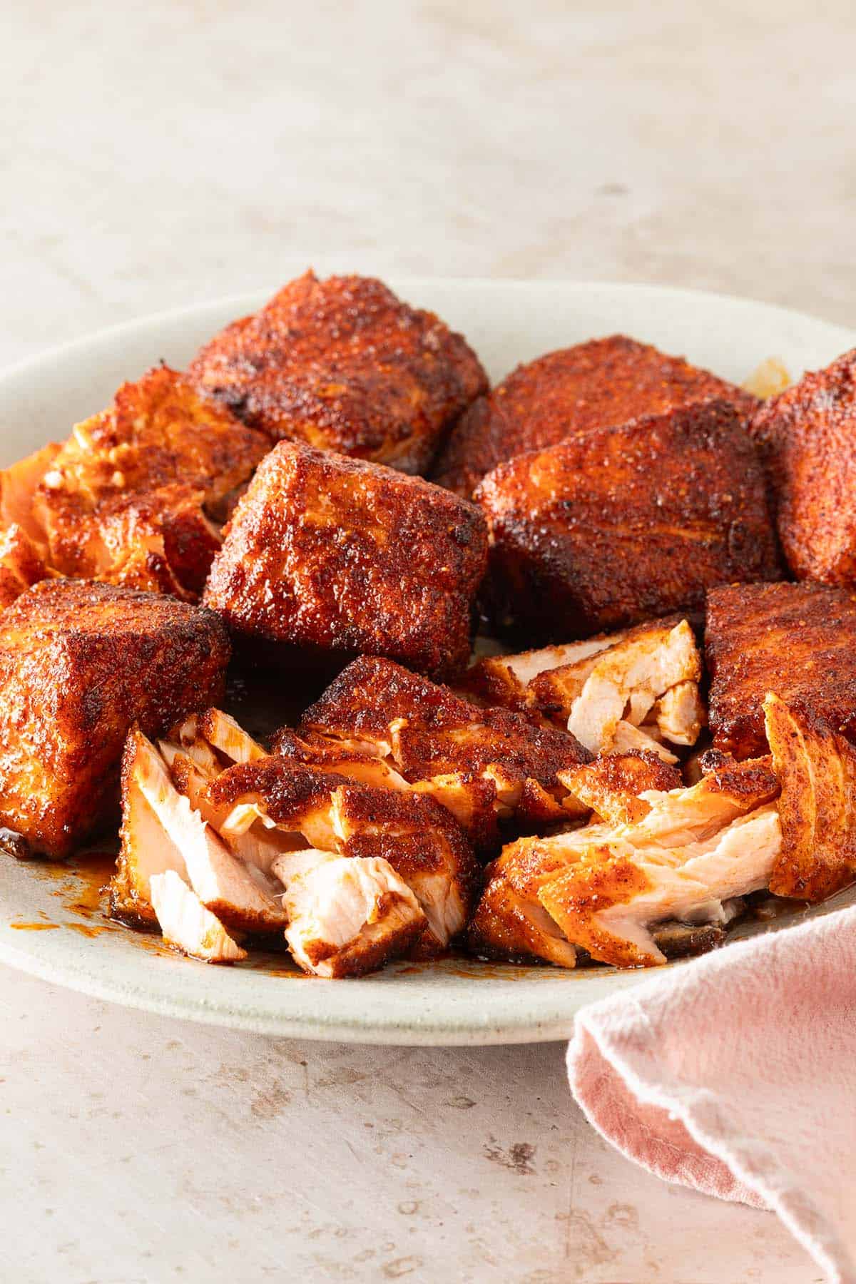 Saftige, w&uuml;rzig marinierte Lachsw&uuml;rfel aus dem Airfryer mit knuspriger Kruste auf einem Teller, teilweise aufgeschnitten, sodass das zarte, saftige Innere sichtbar ist.