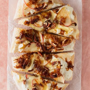 Pinsa Bianca mit Ricotta, geschmolzenem Brie, d&uuml;nnen Apfelscheiben, gebratenen Schalotten und Pekann&uuml;ssen, in St&uuml;cke geschnitten serviert.