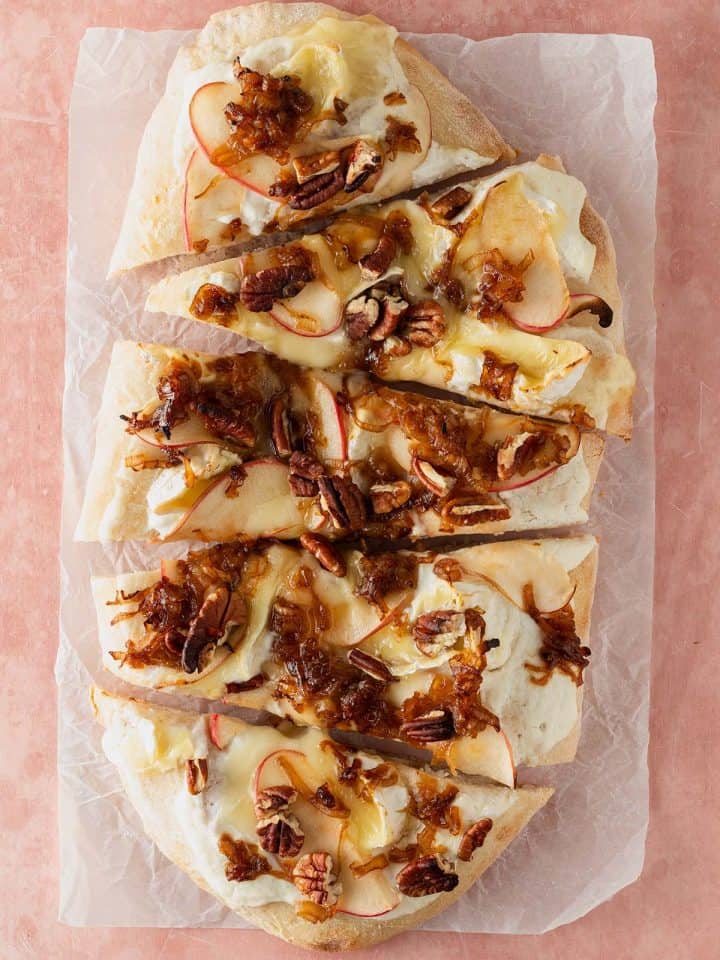 Pinsa Bianca mit Ricotta, geschmolzenem Brie, dünnen Apfelscheiben, gebratenen Schalotten und Pekannüssen, in Stücke geschnitten serviert.