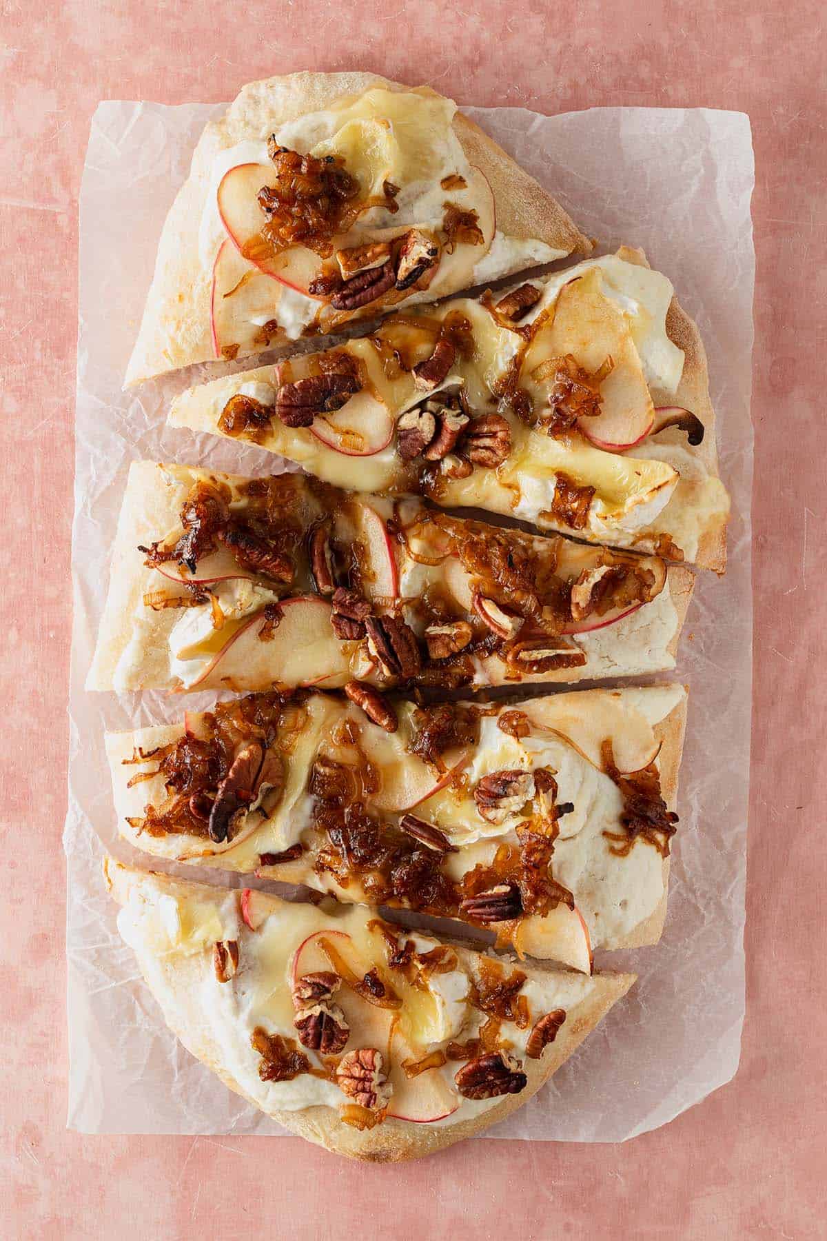Pinsa Bianca mit Ricotta, geschmolzenem Brie, d&uuml;nnen Apfelscheiben, gebratenen Schalotten und Pekann&uuml;ssen, in St&uuml;cke geschnitten serviert.