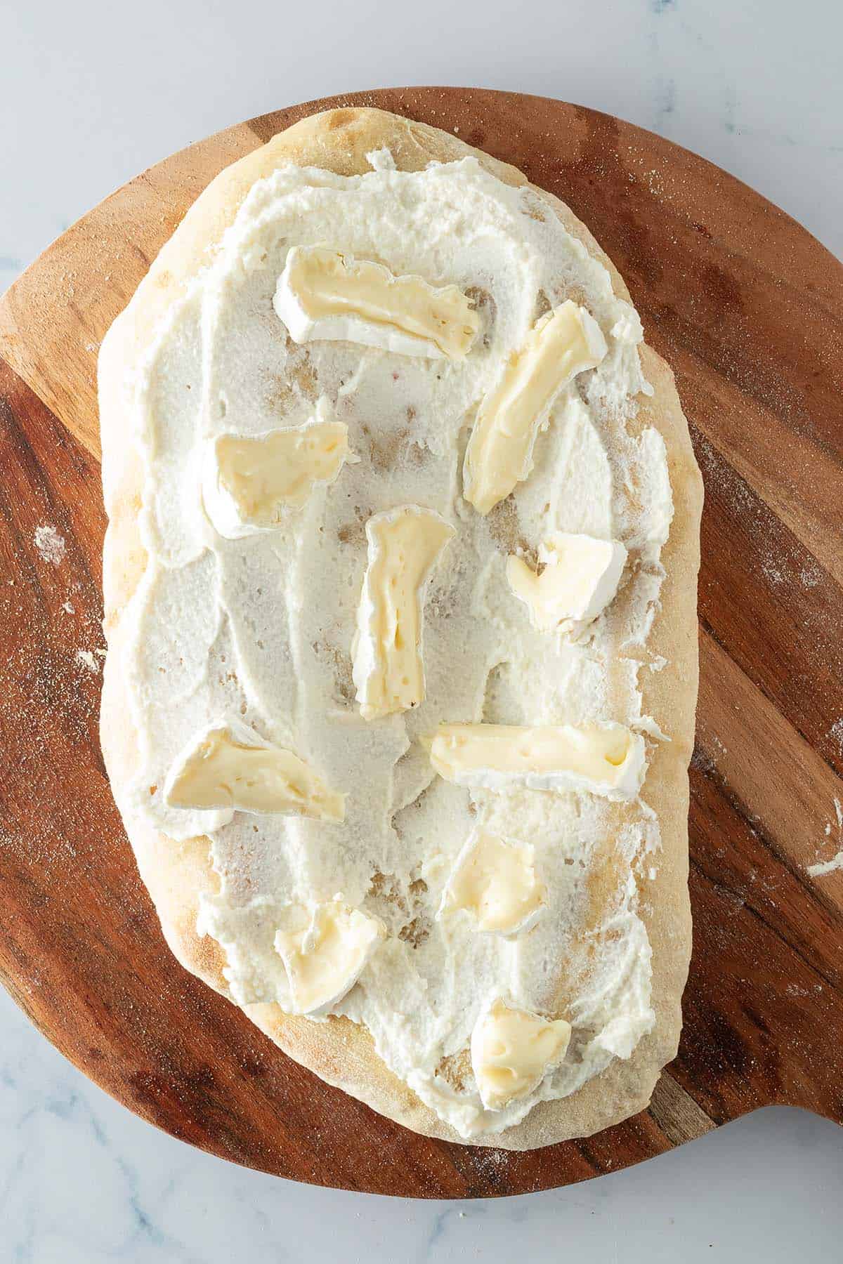 Pinsa Boden mit Ricotta bestrichen und mit Brie belegt.