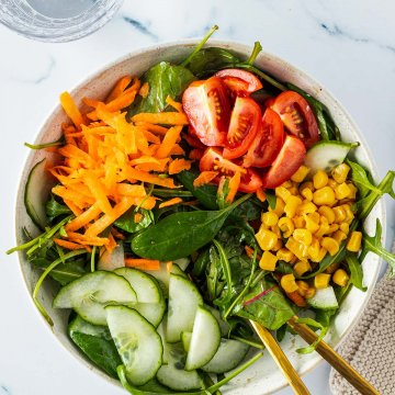 Beilagensalat mit grünem Salat, geraspelten Karotten, Tomaten, Mais und Gurken. Deko am Bildrand.