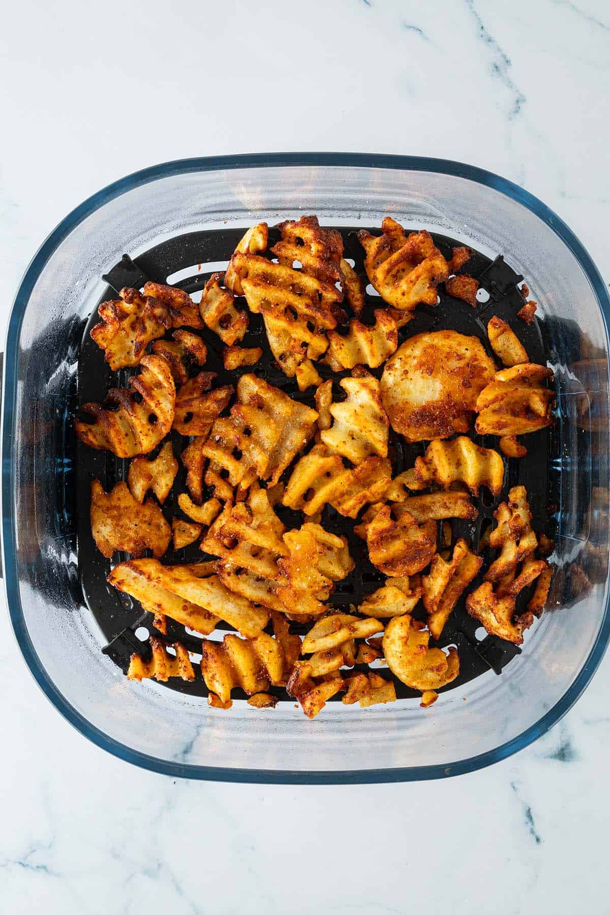 Knusprige Waffelpommes in einem Airfryer-Korb.