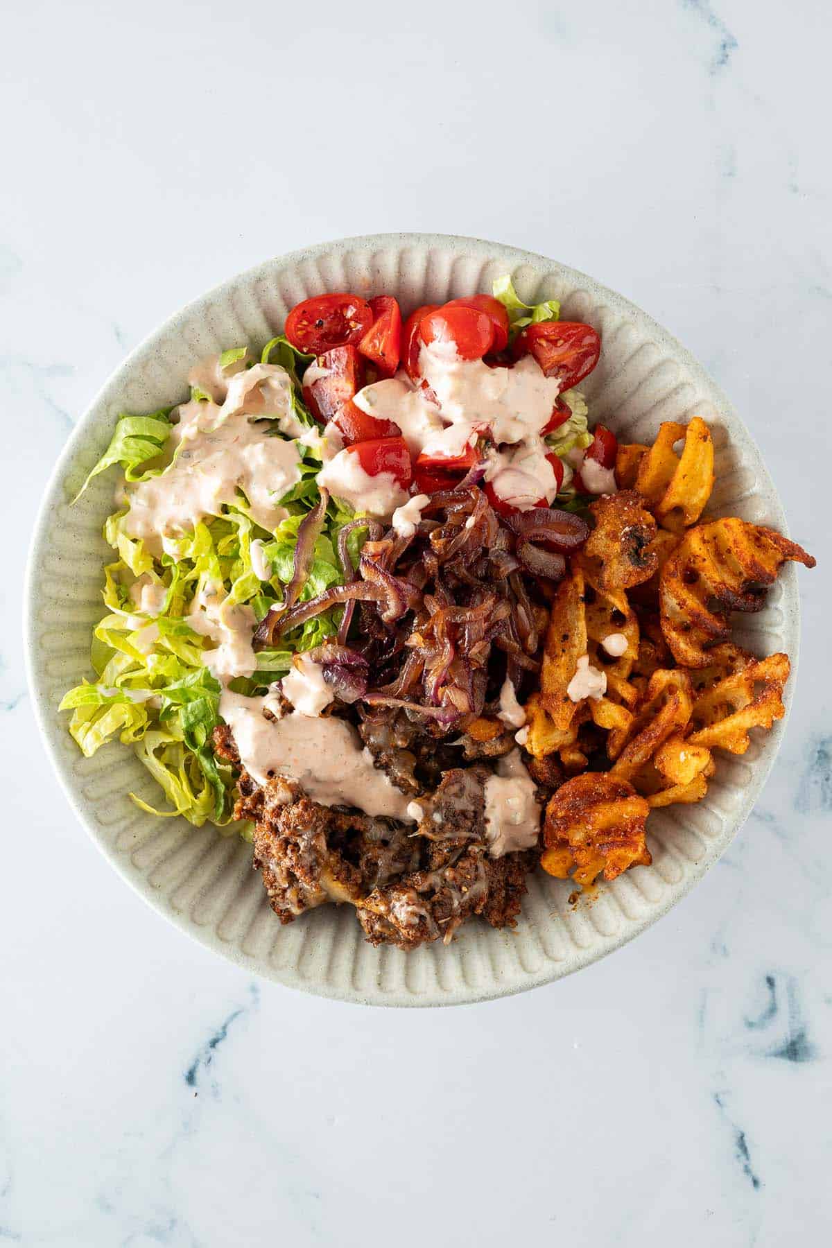 Fertig angerichtete Big Mac Bowl mit Hackfleisch, Waffelpommes, Tomaten, Romana-Salat, knusprigen Zwiebeln und Burgersauce.