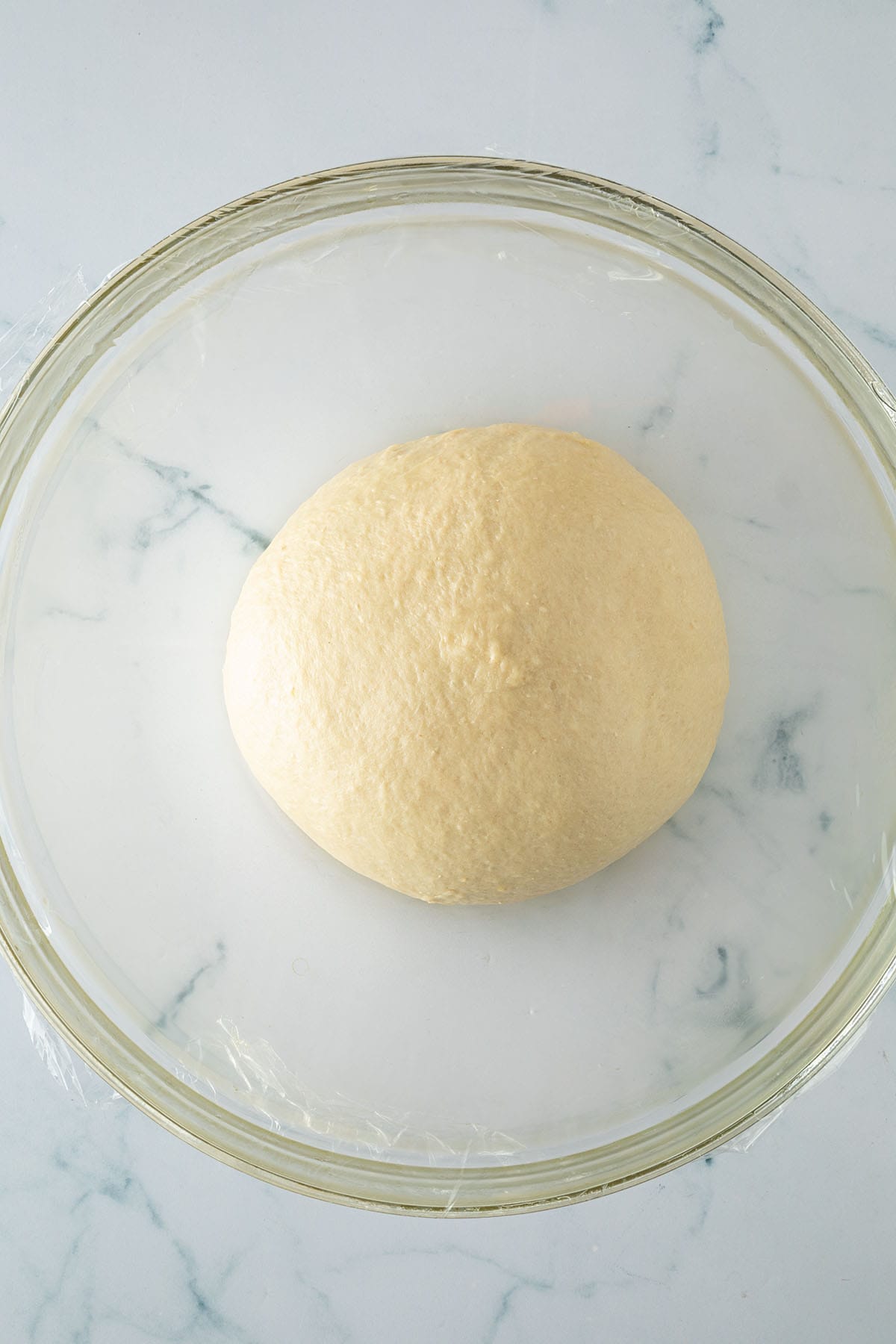 Glatter elastischer Brioche-Teig nach dem Kneten zu einer Kugel geformt, der mit Frischhaltefolie abgedeckt in einer gro&szlig;en Sch&uuml;ssel liegt vorm Gehen.