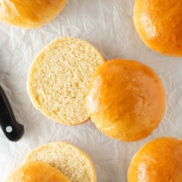 Angeschnittene Brioche Burger Buns mit weicher, fluffiger Krume auf Backpapier neben einem Brotmesser.