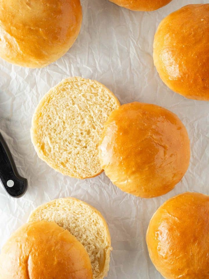 Angeschnittene Brioche Burger Buns mit weicher, fluffiger Krume auf Backpapier neben einem Brotmesser.