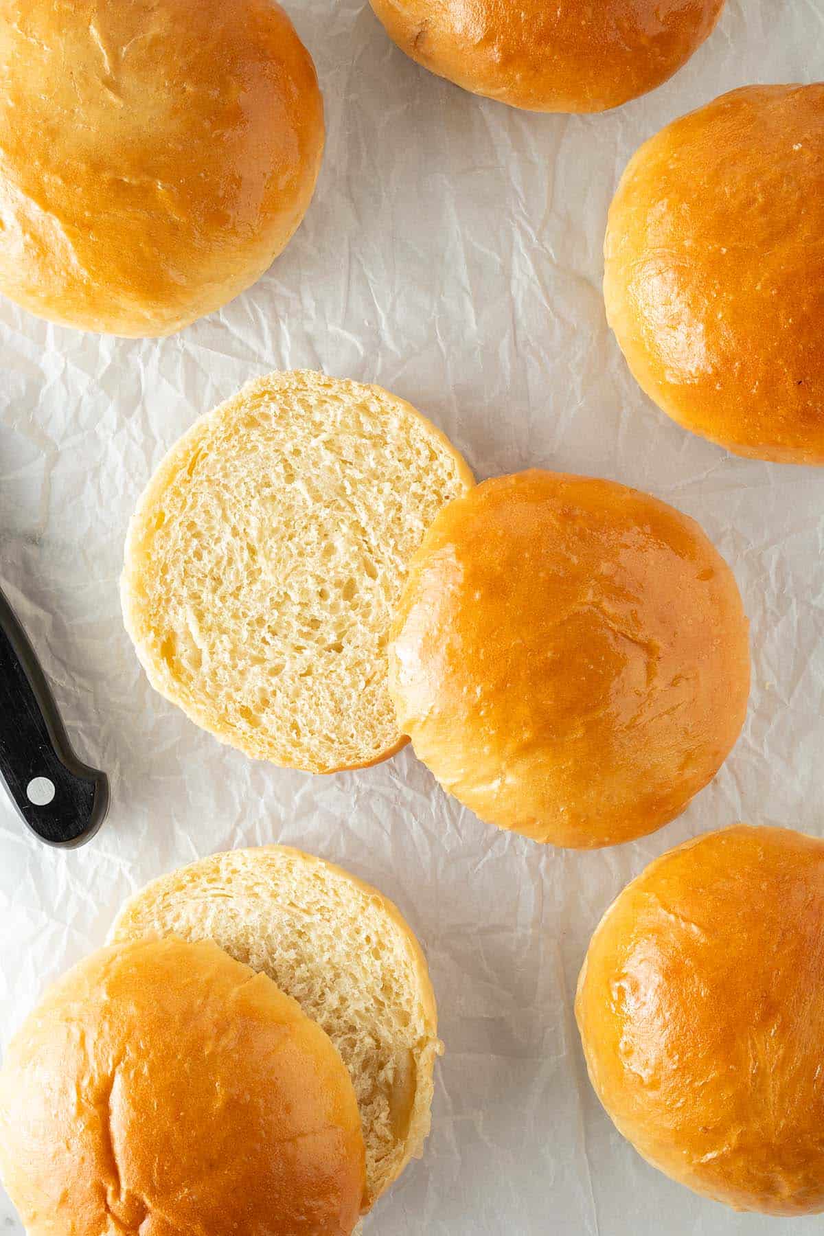 Angeschnittene Brioche Burger Buns mit weicher, fluffiger Krume auf Backpapier neben einem Brotmesser.