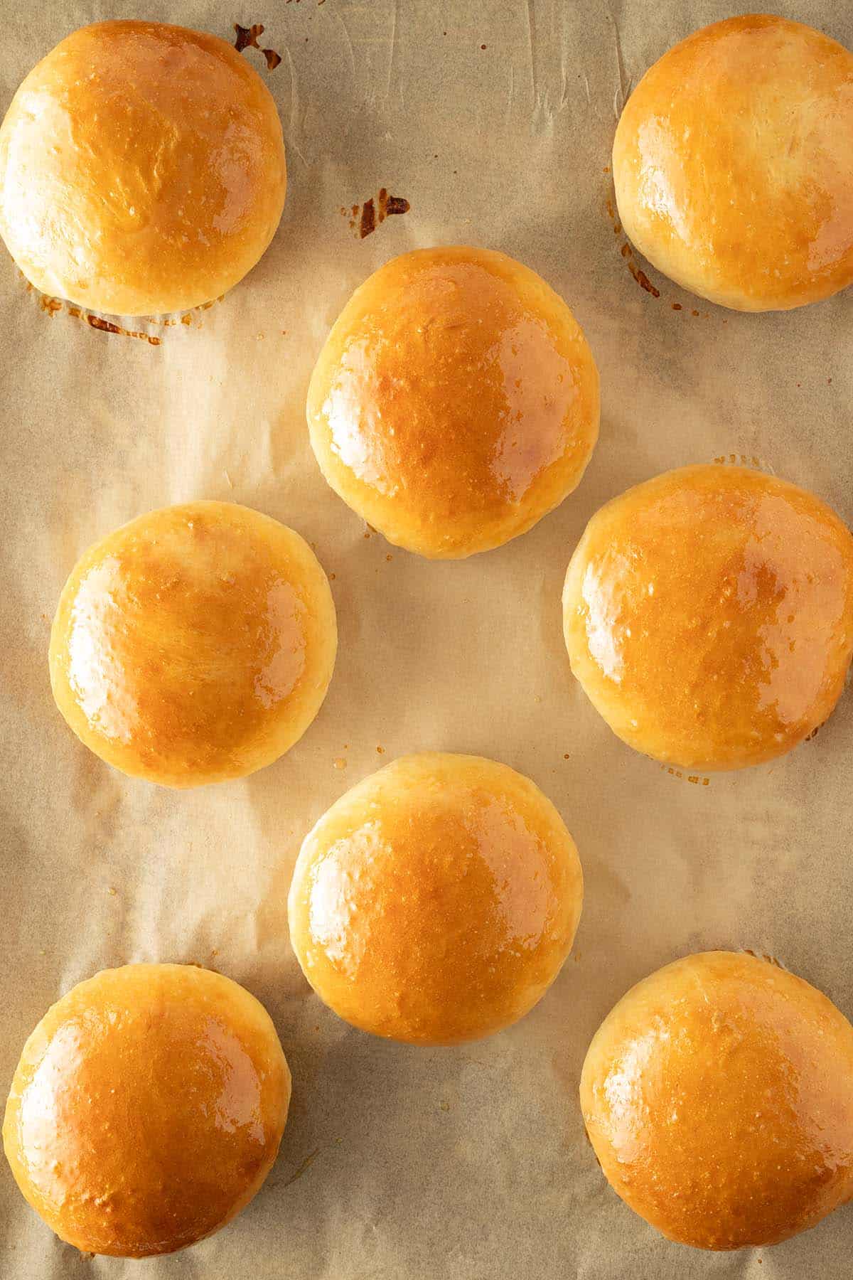 Frisch gebackene Brioche Burger Buns mit einer gl&auml;nzender, mit Butter bestrichenen goldbrauner Kruste auf einem mit Backpapier ausgelegten Backblech.