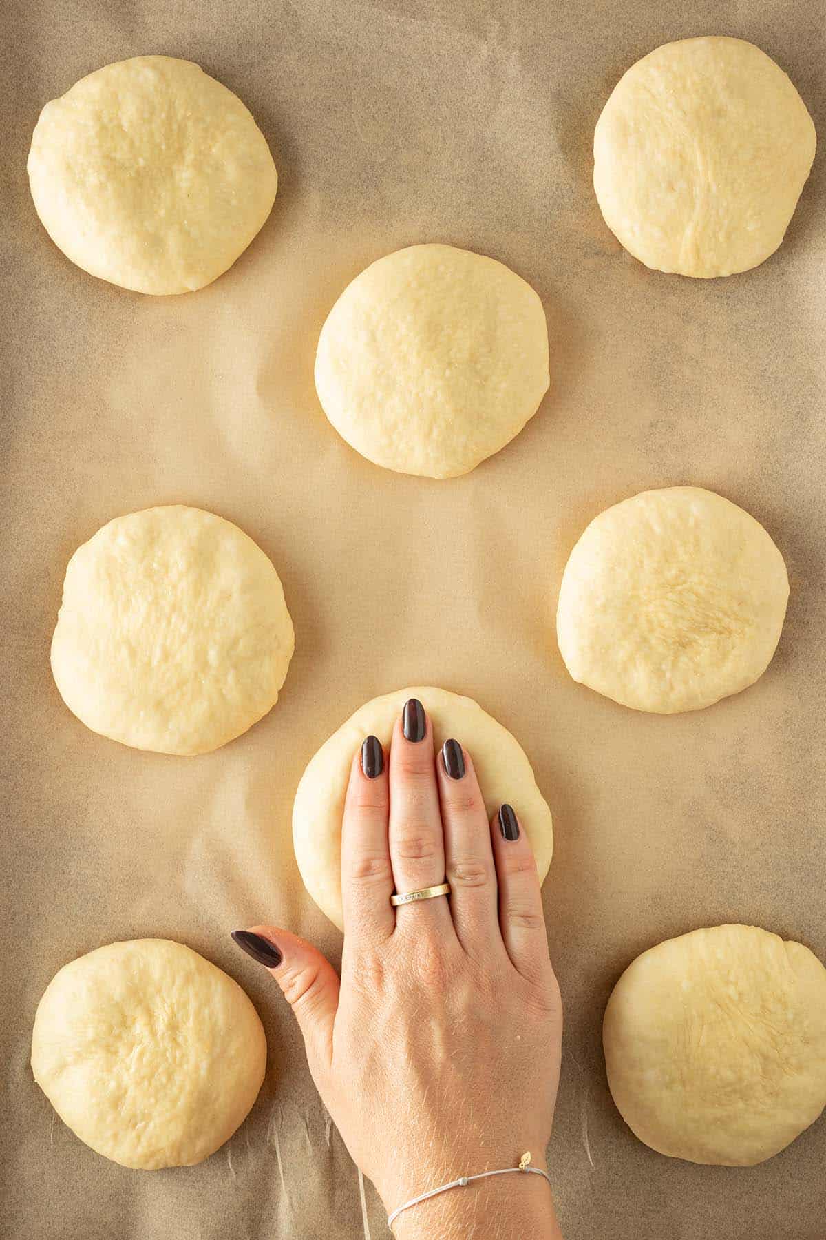 Die zu Kugeln geformten Burger Buns werden mit einer falschen Hand auf dem Backblech flach gedr&uuml;ckt.