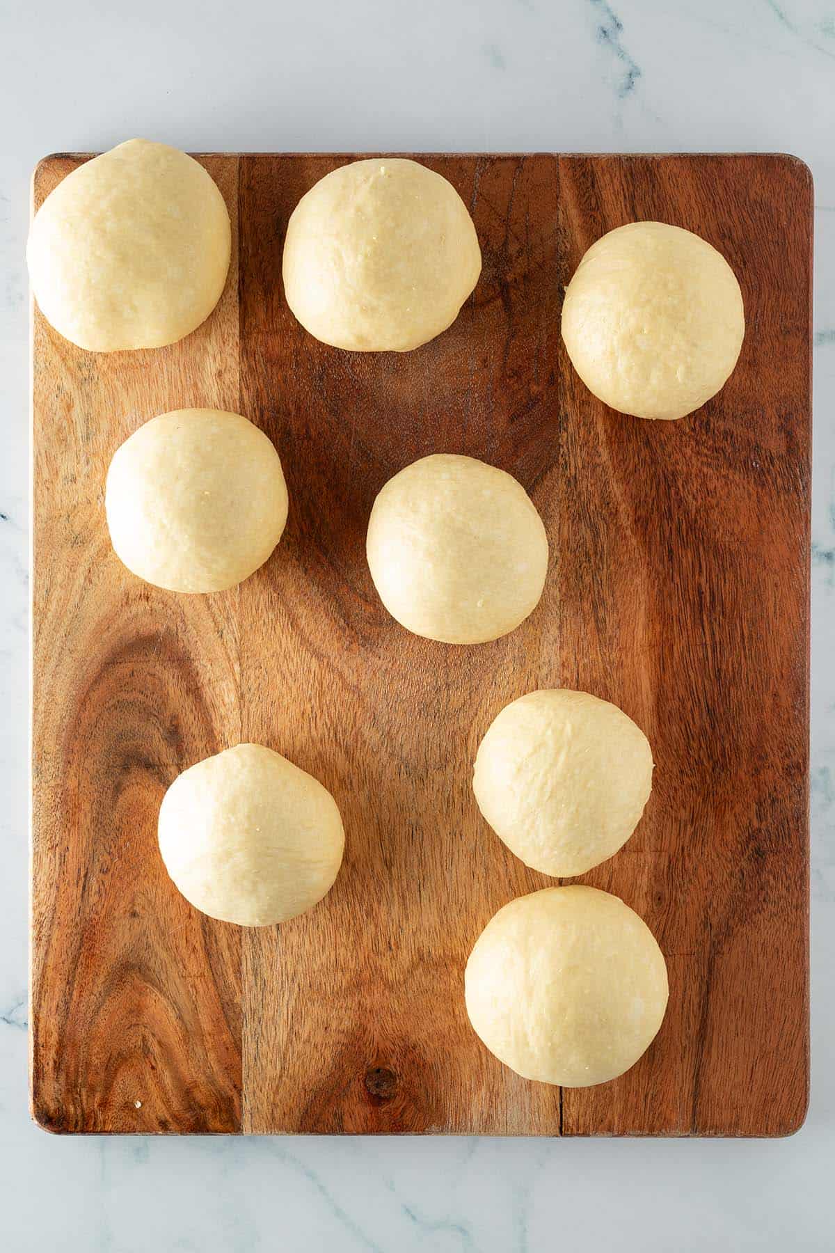 Brioche Teig zu 8 Kugeln geformt auf einen Holzbrett.