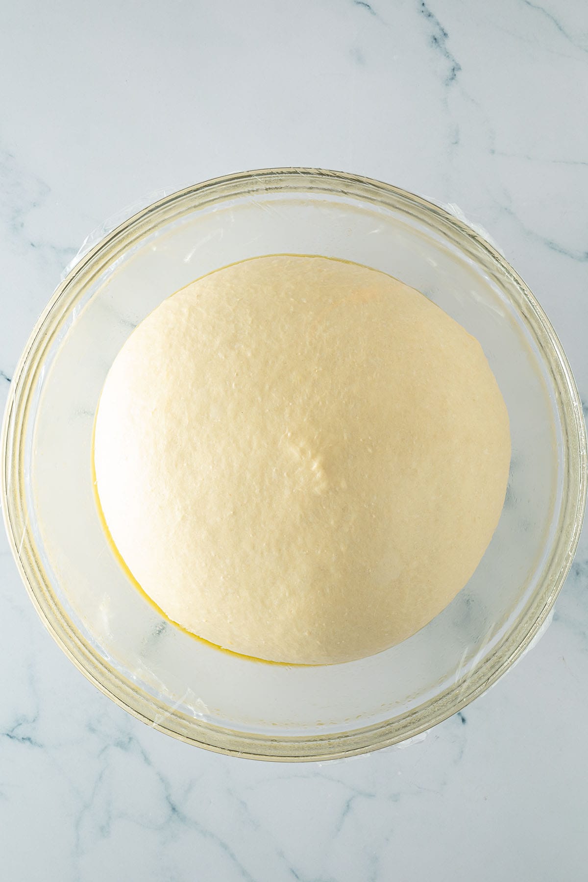 Brioche-Teig nach dem Gehen in einer mit Frischhaltefolie abgedeckten Glassch&uuml;ssel.