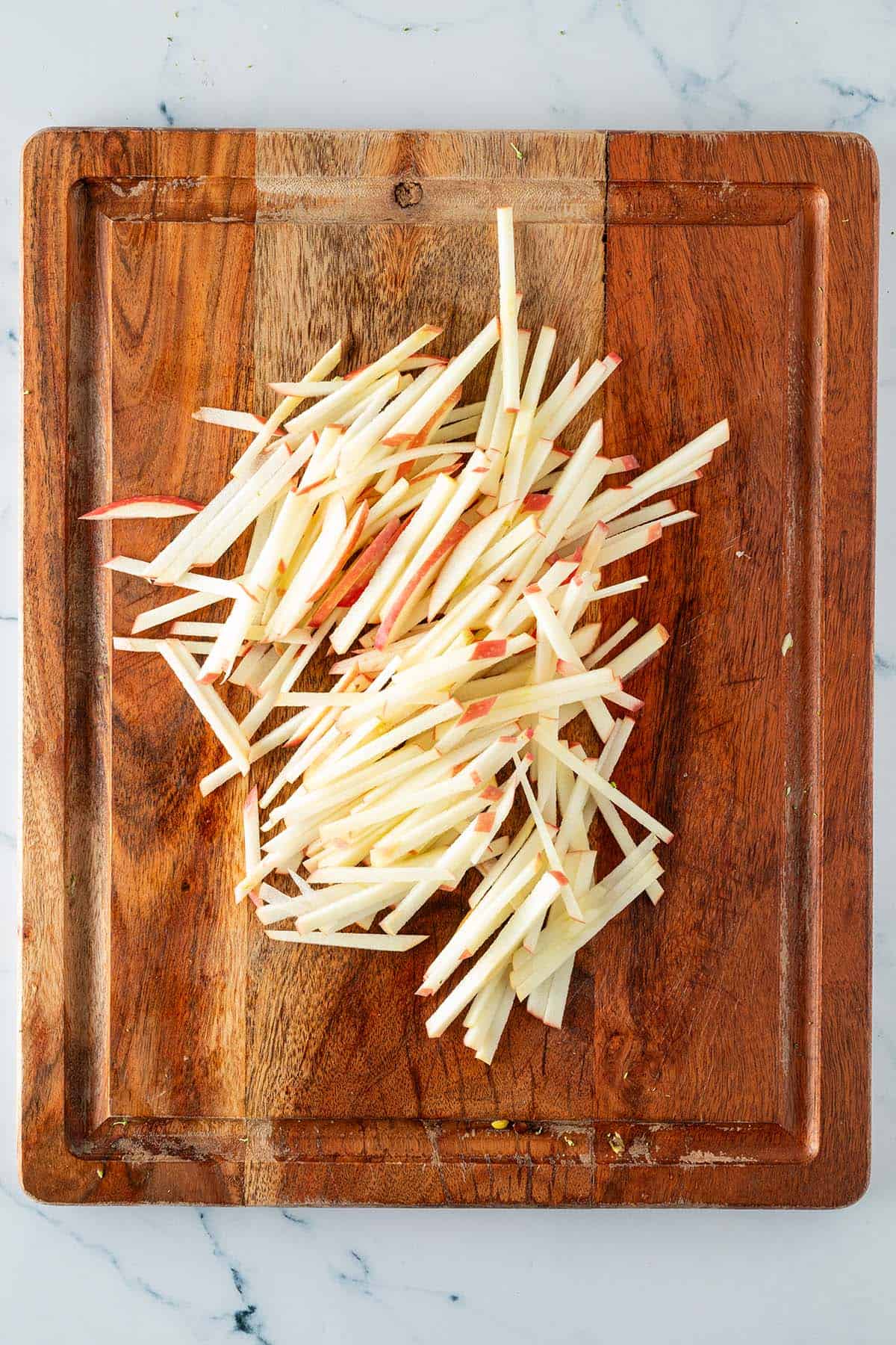 In d&uuml;nne Stifte geschnittener Apfel auf einem Holzbrett.