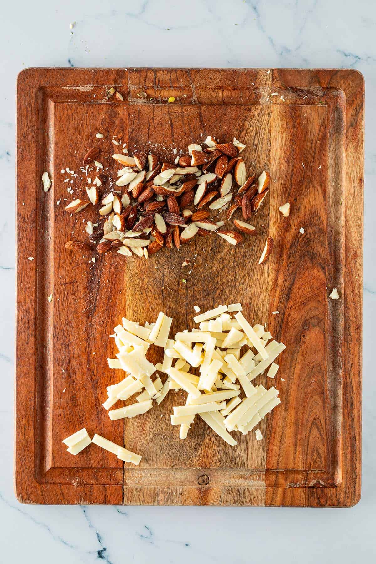 Grob gehackte Mandeln und in kleine Streifen geschnittener Schnittk&auml;se auf einem Brett.