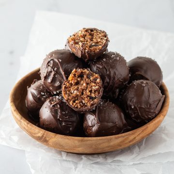 Mehrere ganze und halbierte, mit Schokolade überzogene Brownie Energy Balls in einer kleinen Holzschüssel.
