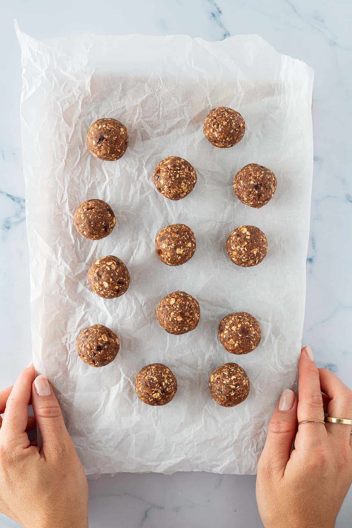 Zu runden Kugeln geformte Energy Balls auf einem Stück Backpapier.