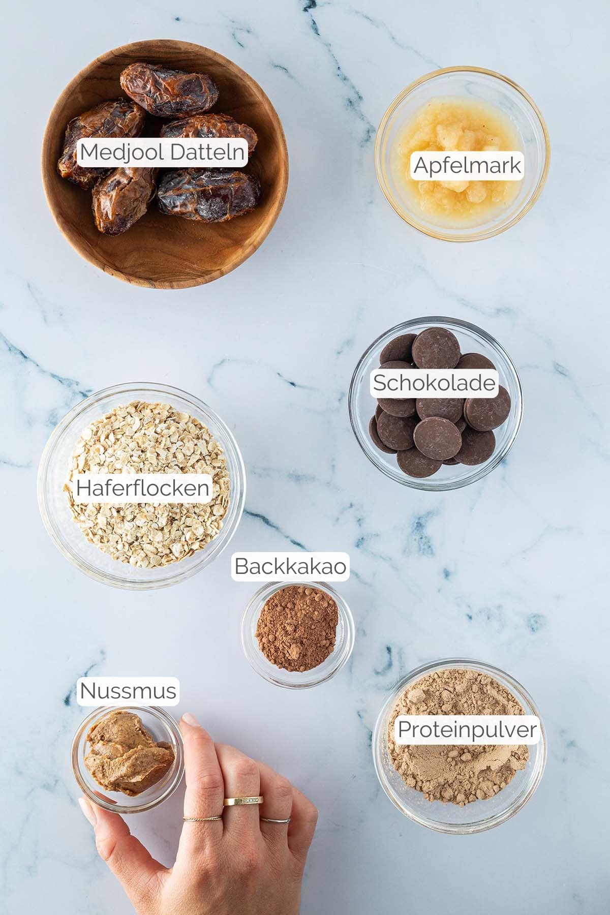 Alle Zutaten mit jeweiligen Textbeschriftungen, die für die Brownie Energy Balls benötigt werden.