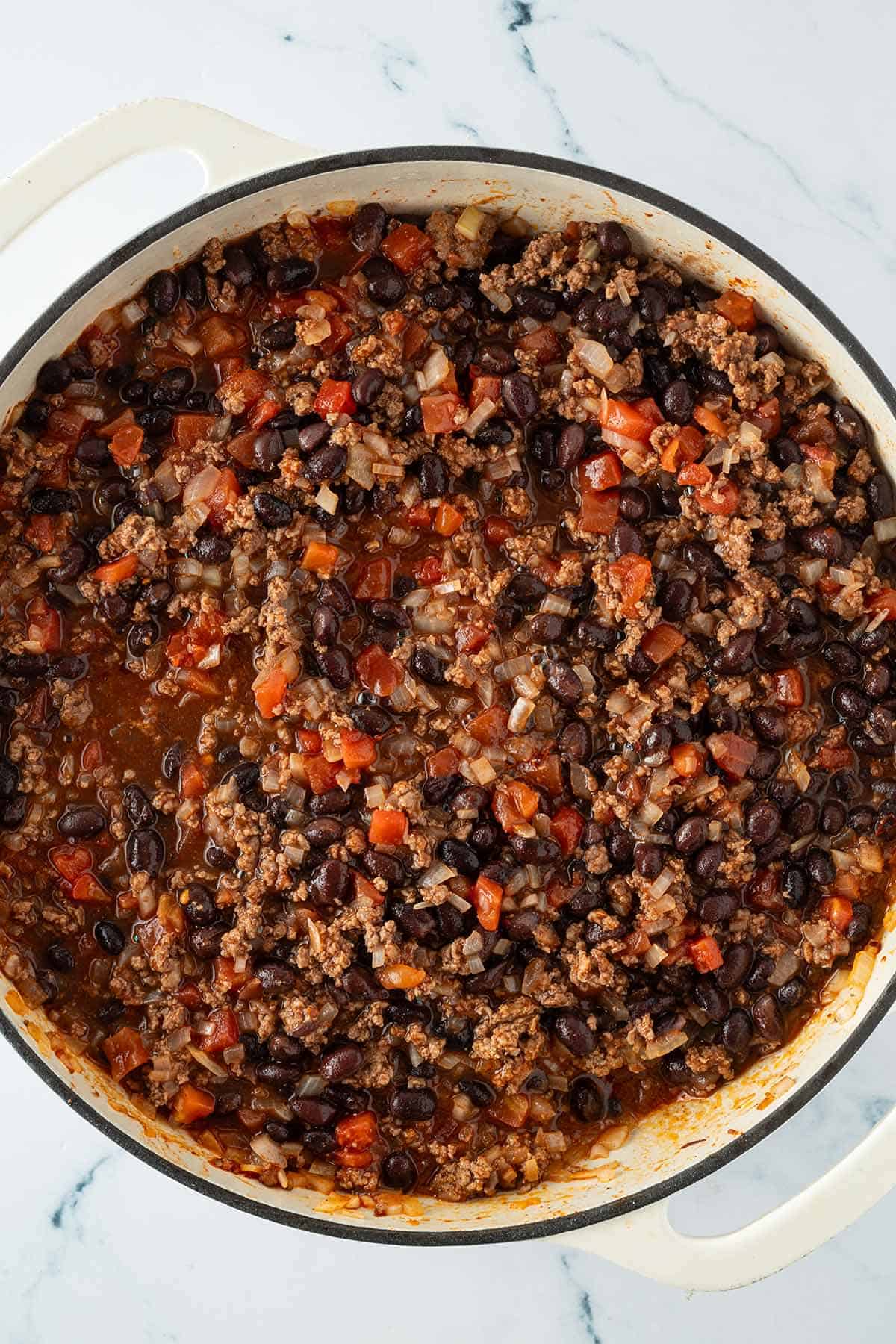 In einer großen Pfanne kochen angebratenes Hackfleisch und schwarze Bohnen in Tomatensauce.