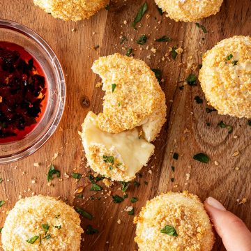 Gebackene Camemberts aus dem Airfryer mit knuspriger Panade auf einem Holzbrett mit Petersilie und Dip.