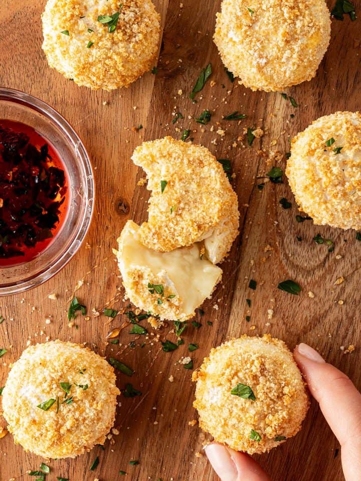 Gebackene Camemberts aus dem Airfryer mit knuspriger Panade auf einem Holzbrett mit Petersilie und Dip.