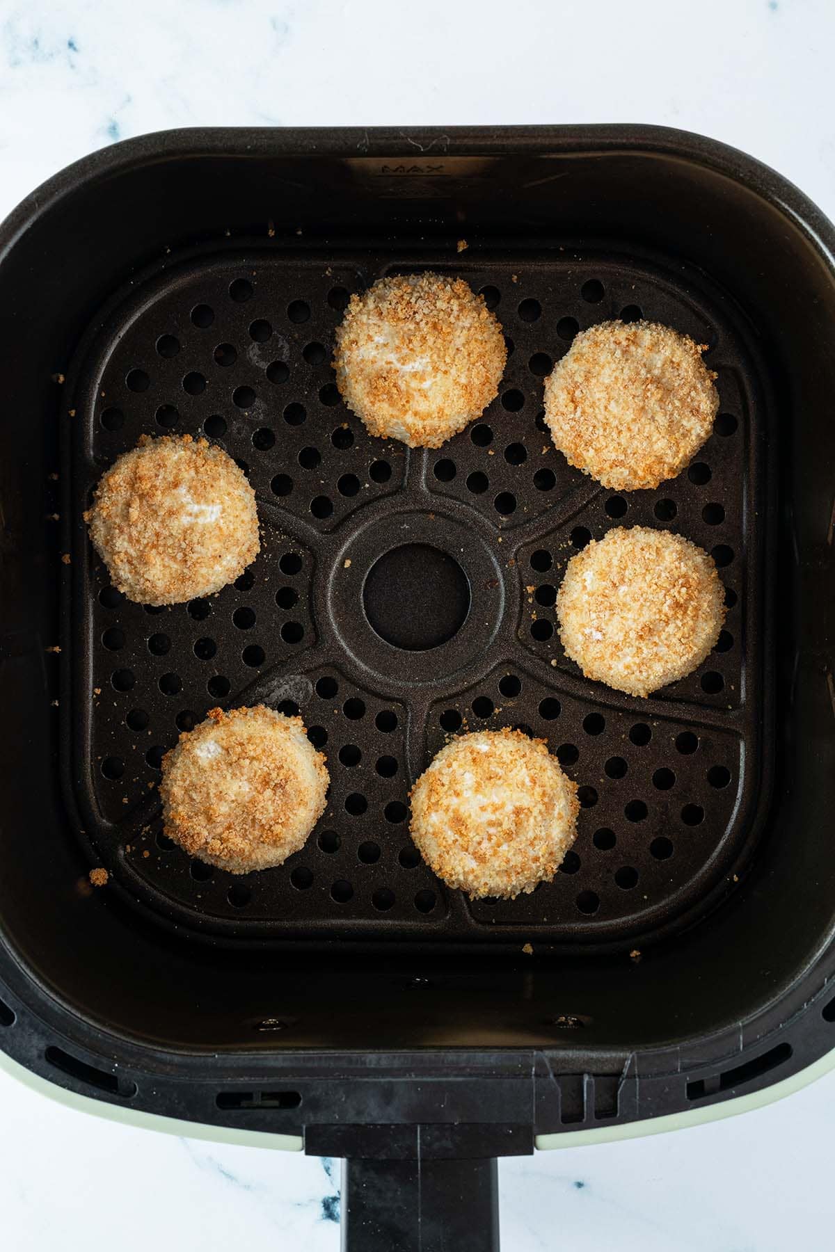 Goldbraun gebackene Mini Camemberts in dem Korb einer Heißluftfritteuse.