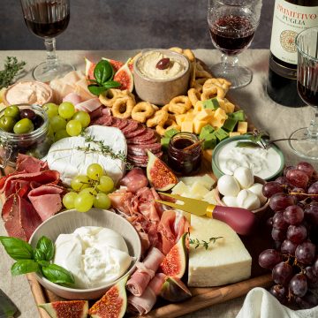 Große Charcuterie-Platte mit Käse, Salami, Schinken, Feigen, Trauben, Crackern, Dips und Rotwein auf einem gedeckten Tisch.