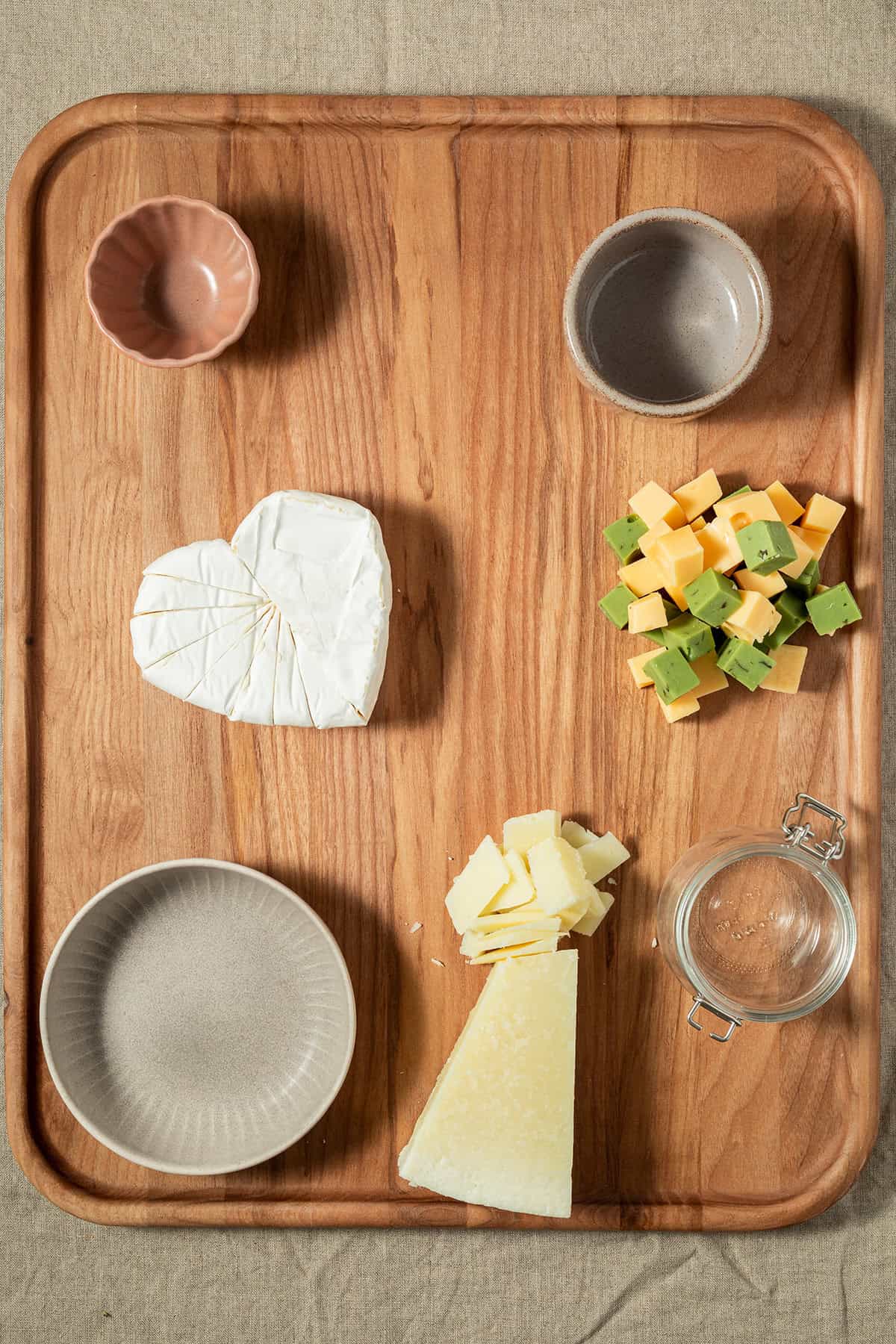 Leeres Holzbrett mit vorbereiteten Schälchen und verschiedenen Käsesorten als Grundlage zum Anrichten einer Charcuterie-Platte.