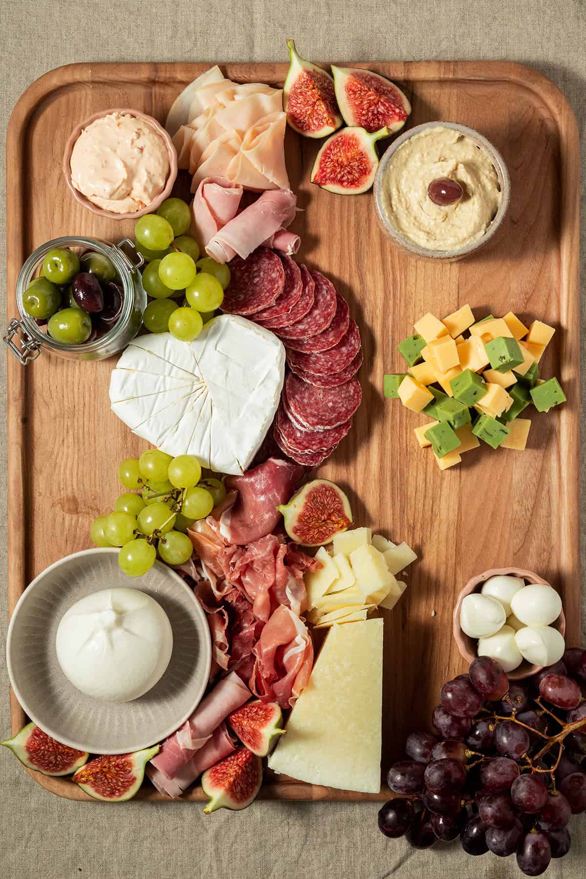 Charcuterie-Platte mit ergänzten Crackern, Käsewürfeln, Joghurt-Dip, Mozzarella-Kugeln und Trauben.