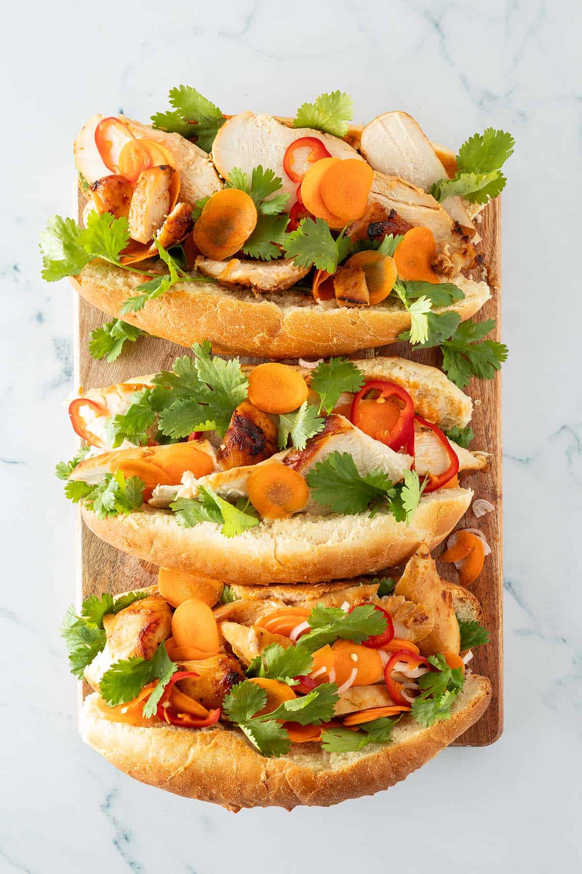 rei Chicken Banh Mi Sandwiches mit Hähnchen, Gemüse und Koriander auf weißem Hintergrund.