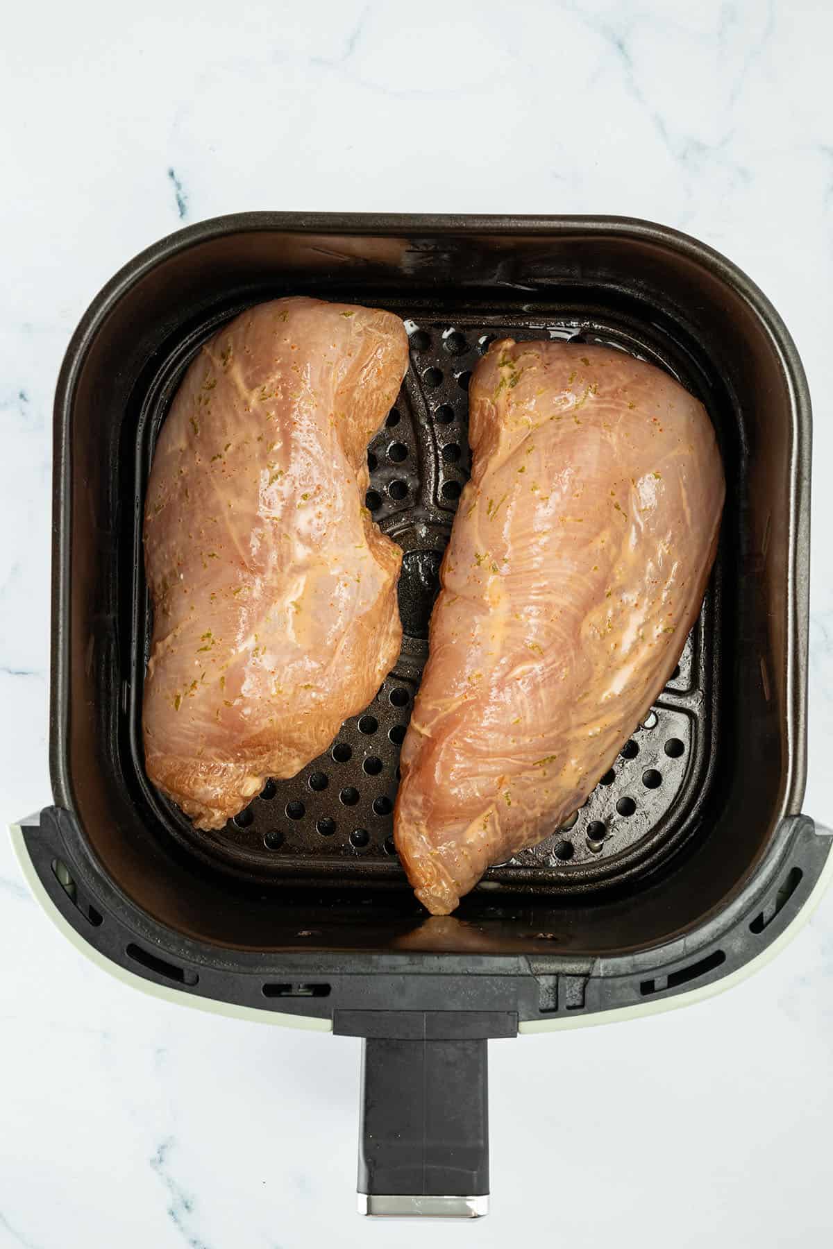Zwei marinierte Hähnchenbrustfilets im Airfryer-Korb vor dem Garen.