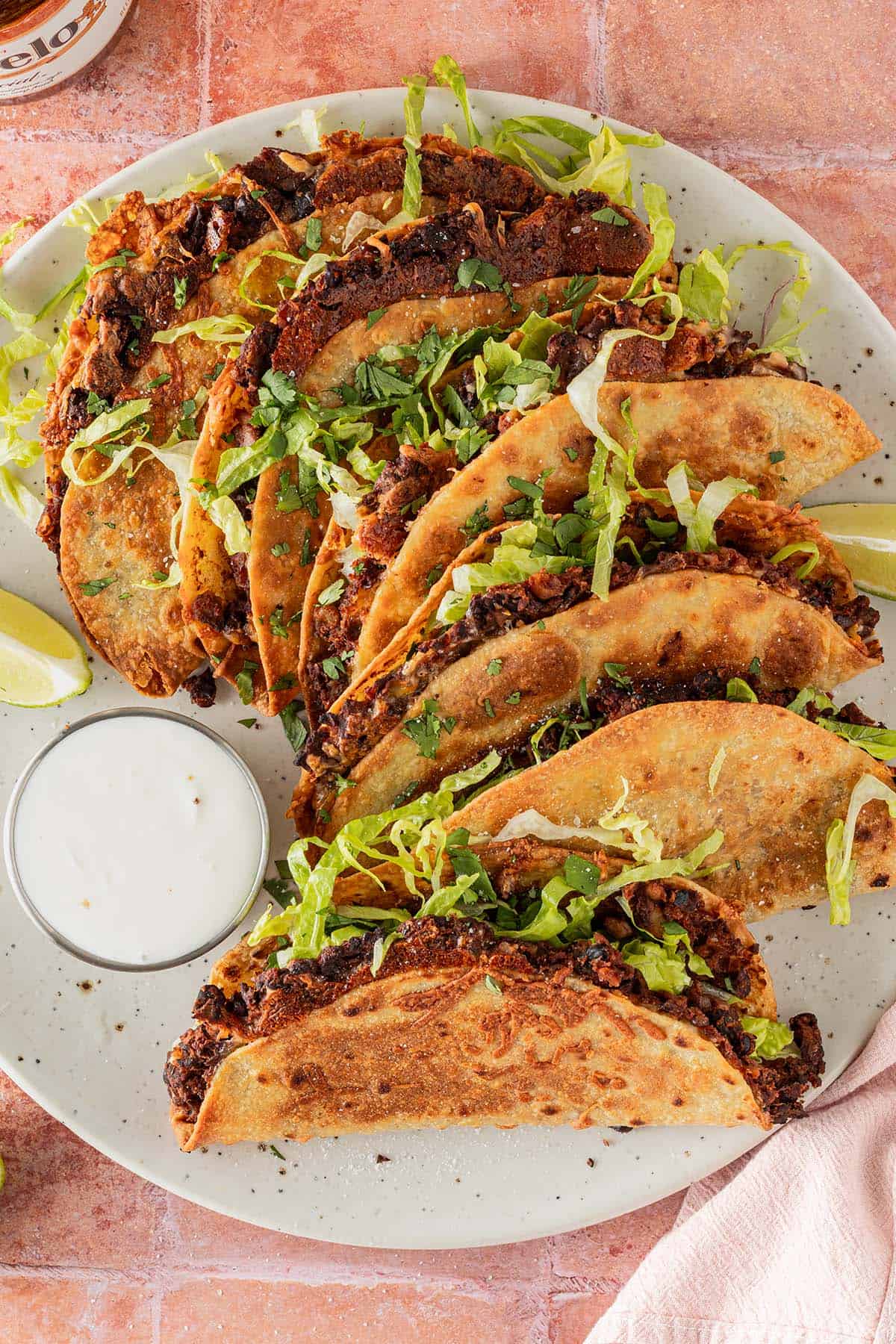 Teller mit knusprigen Crispy Tacos mit schwarzen Bohnen, Salat und Dip von oben fotografiert.