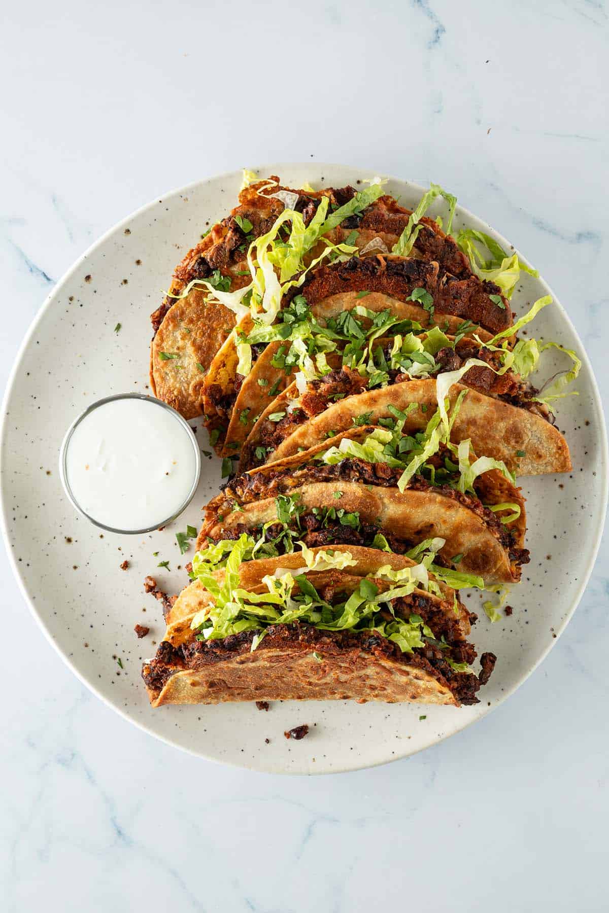 Crispy Tacos mit schwarzen Bohnen und Salat auf einem Teller mit Dip.