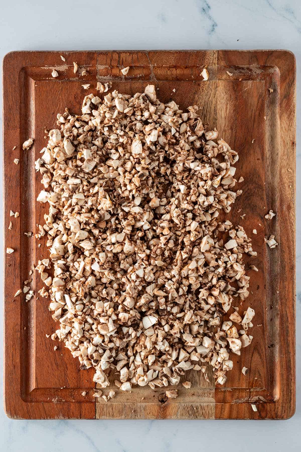 Fein gehackte Champignons auf einem Holzbrett.