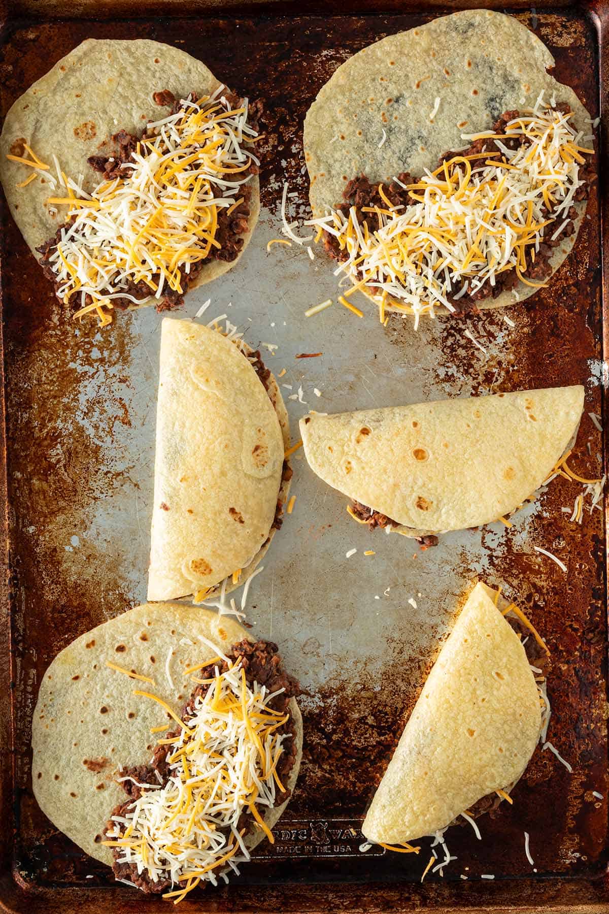 Tortillas mit schwarzer Bohnenfüllung und Käse gefüllt und teilweise zusammengeklappt auf einem Blech.