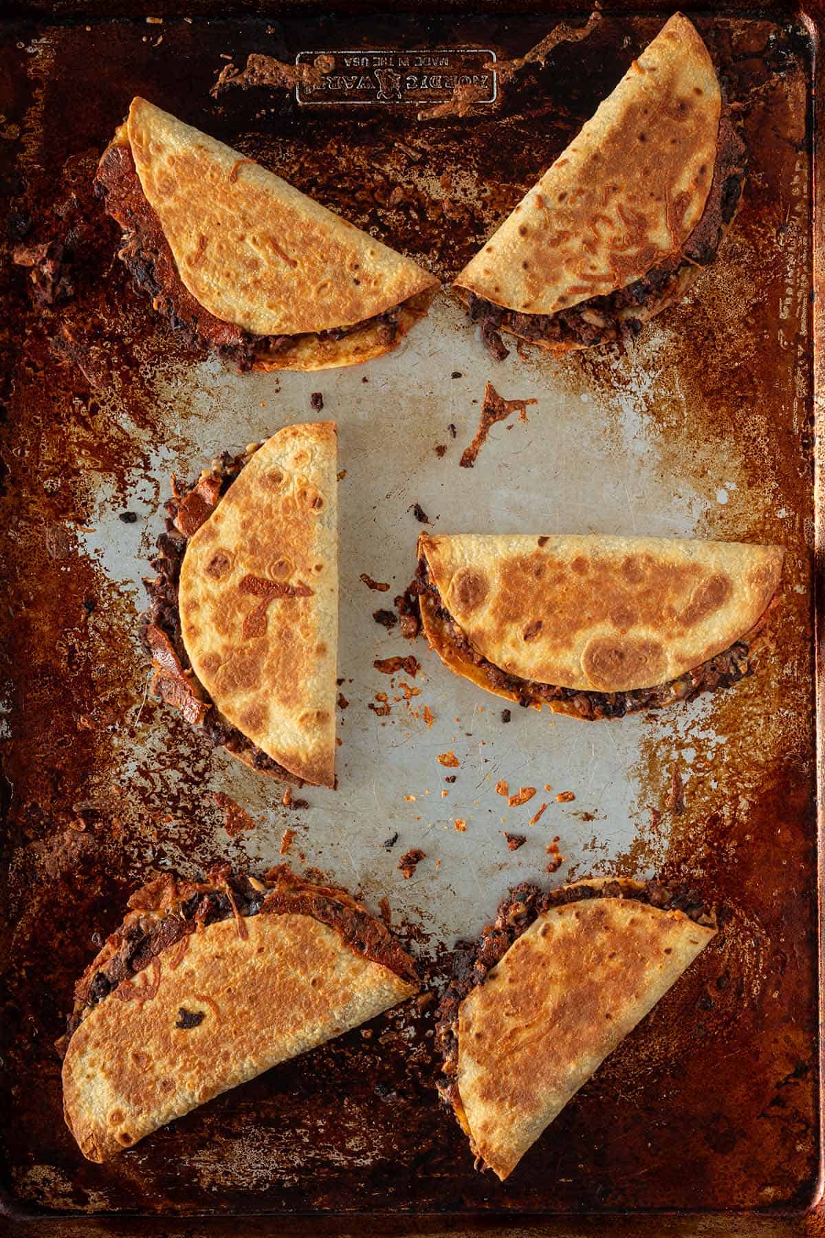 Goldbraun gebackene Crispy Tacos mit schwarzer Bohnenfüllung auf einem Backblech.