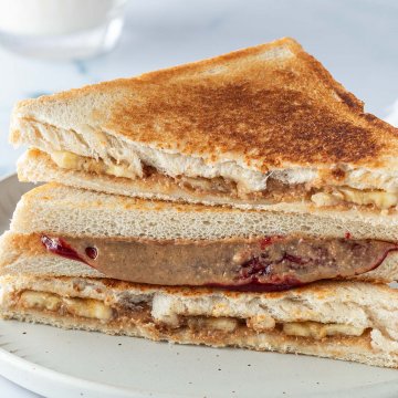 Stapel aus drei Sandwiches, die mit Erdnussbutter und Banane oder mit Erdnussbutter und Marmelade gefüllt sind.