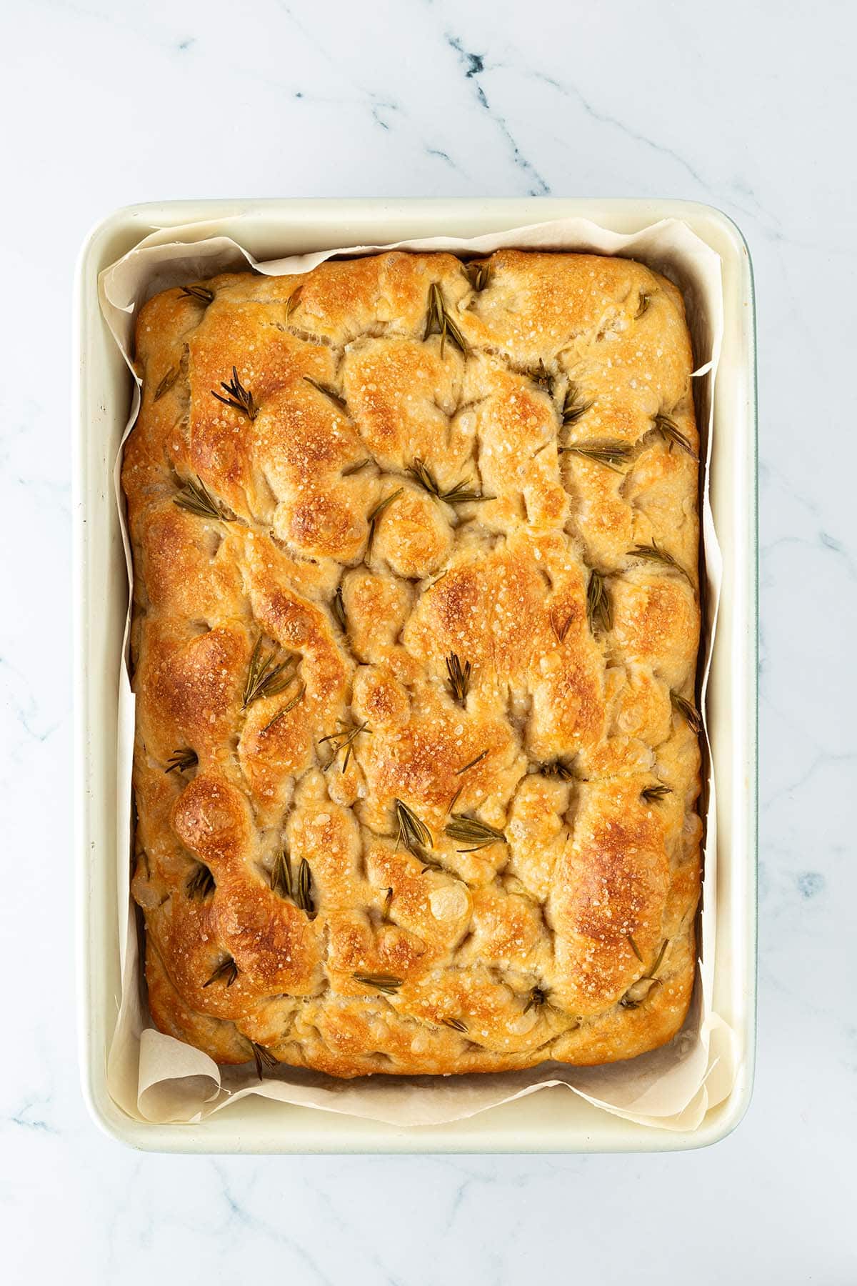 Frisch gebackenes goldbraunes Focaccia mit Rosmarin und grobem Salz in einer rechteckigen Backform.