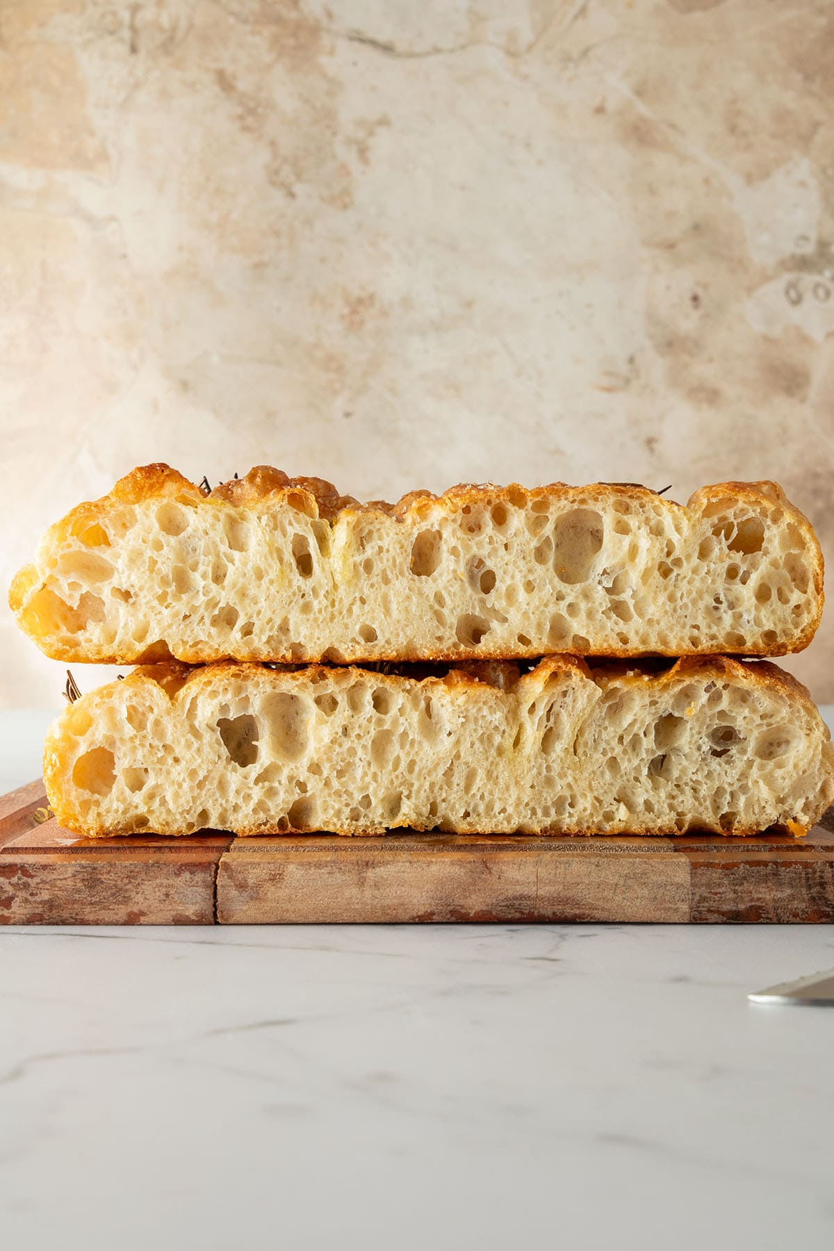 Aufgeschnittene Focaccia mit goldbrauner Kruste und luftiger, großporiger Krume auf einem Holzbrett.