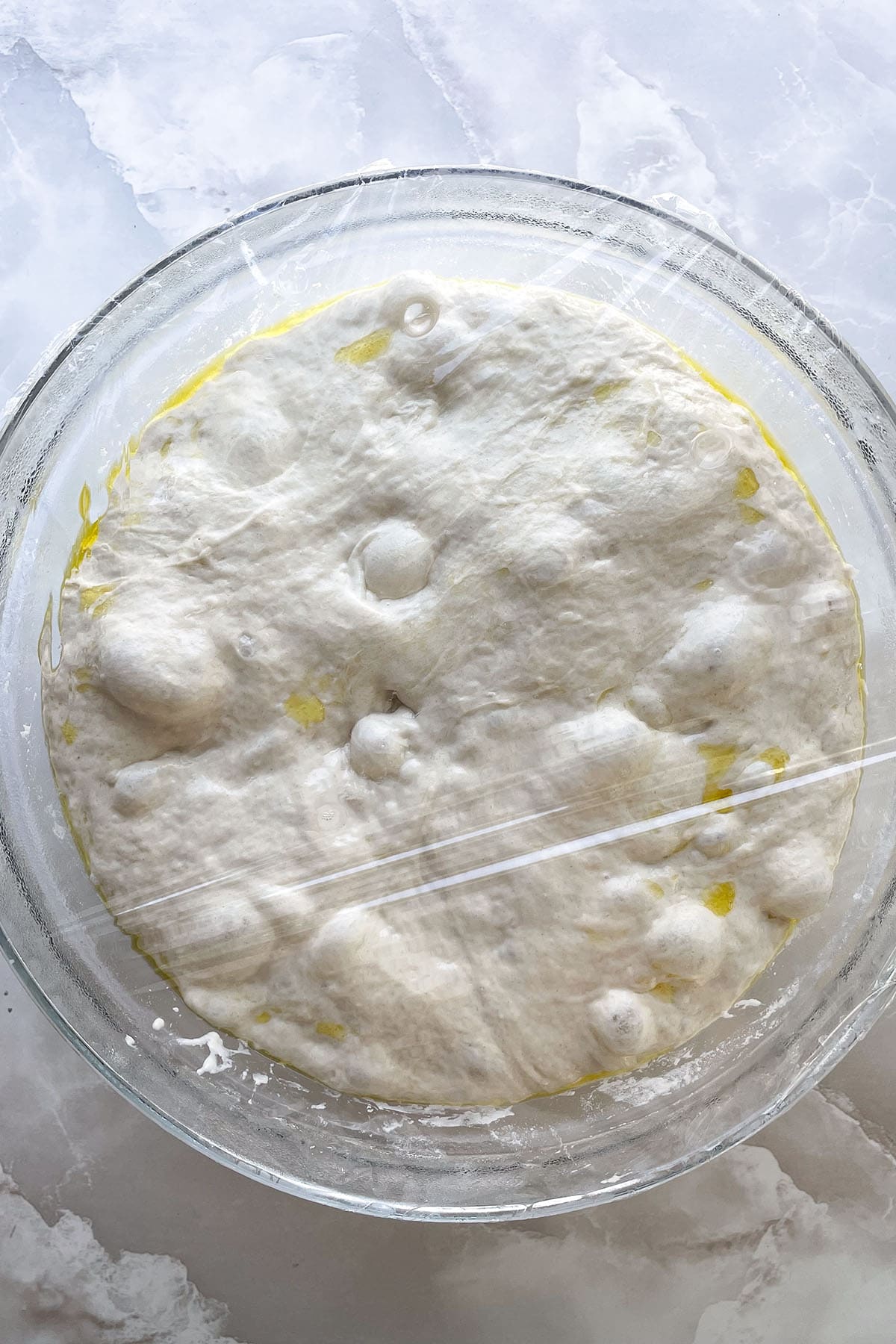 Luftig aufgegangener Focaccia-Teig mit sichtbaren Luftblasen und Olivenöl nach der Gehzeit im Kühlschrank.