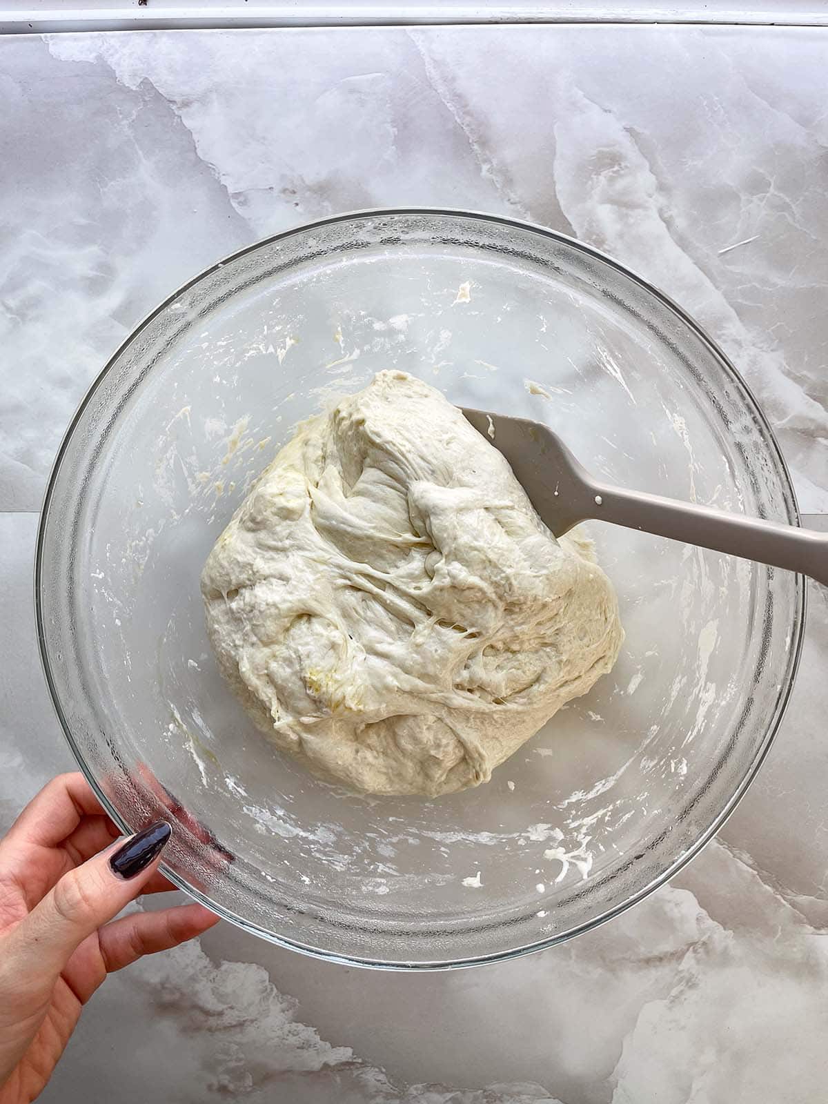 Focaccia-Teig wird nach dem Gehen mit einem Teigschaber von der Schüssel abgelöst.