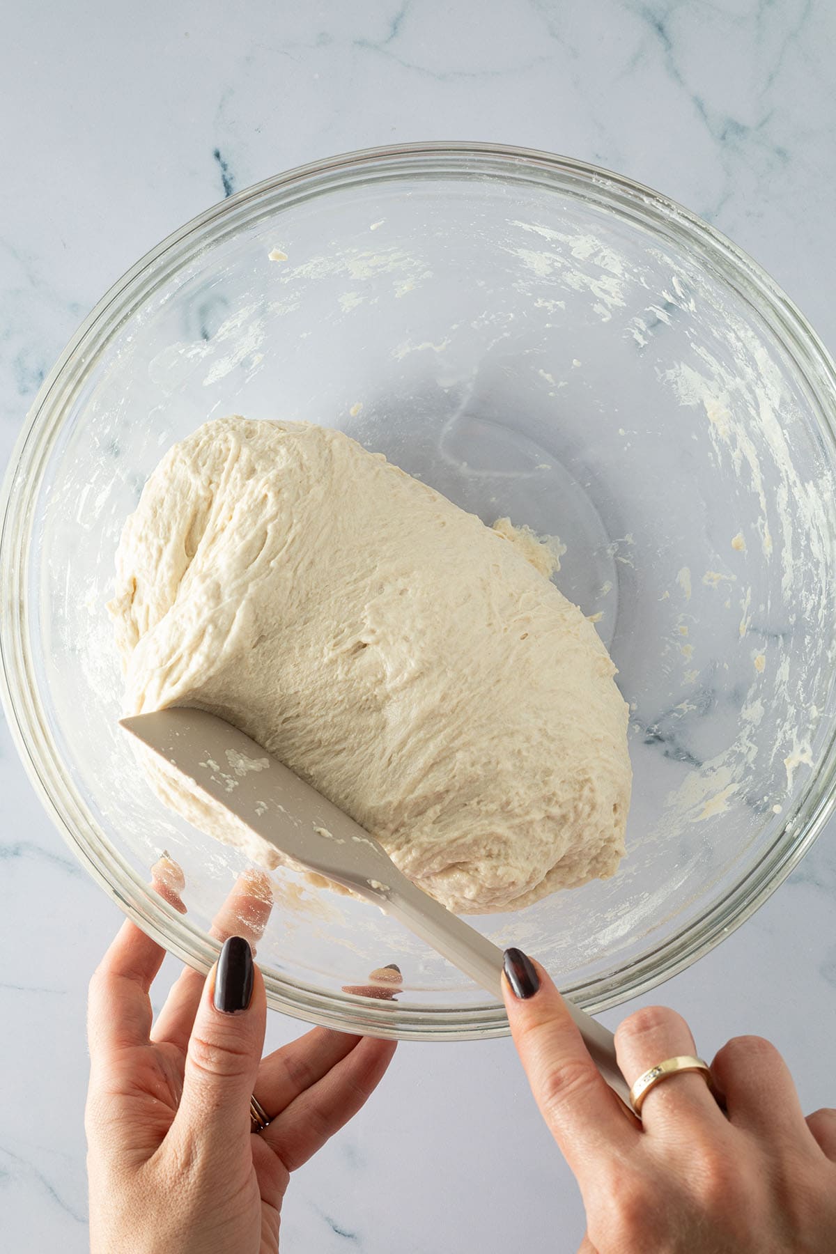 Focaccia-Teig wird nach 30 Minuten mit einem Teigschaber in einer Glasschüssel gefaltet.