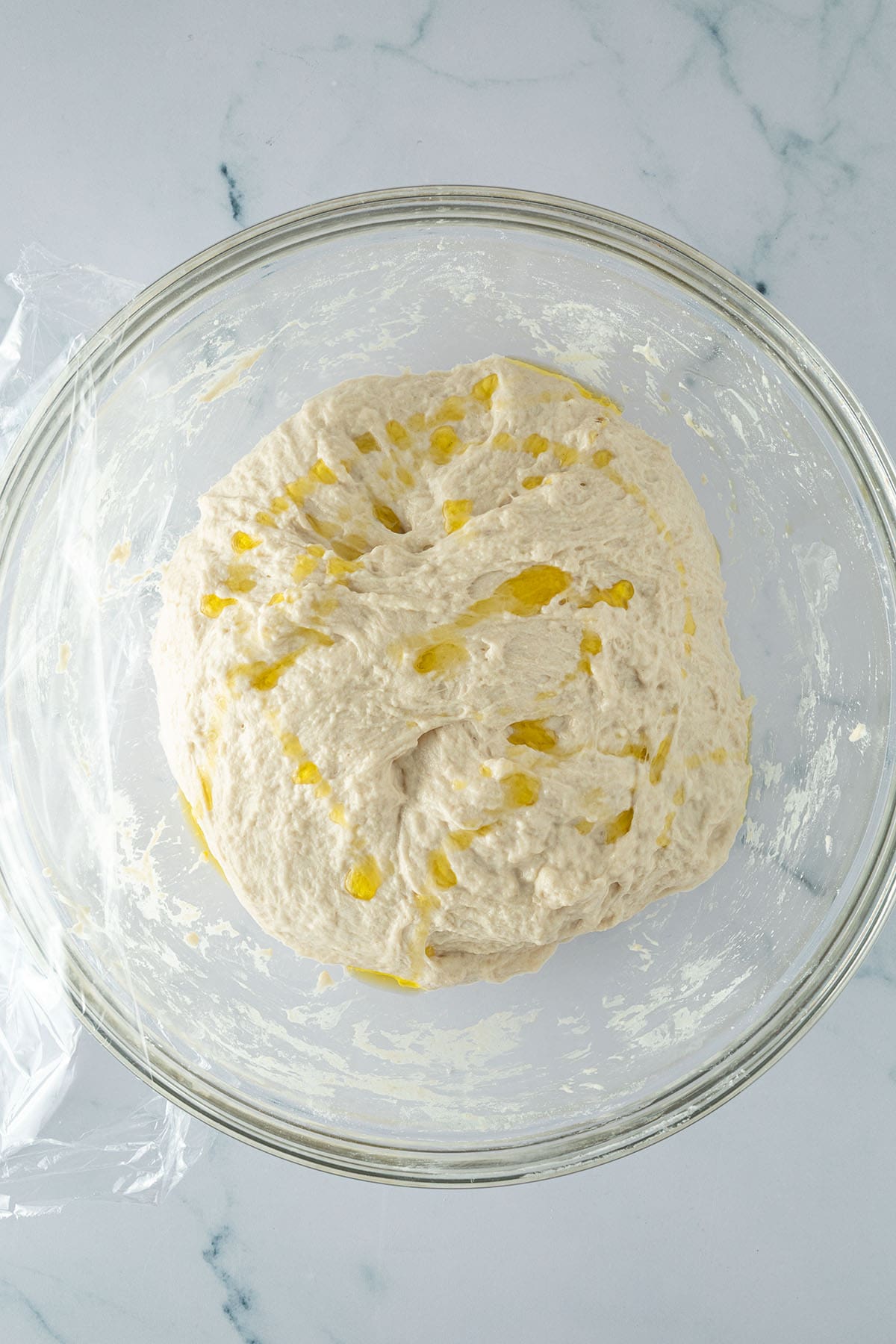 Focaccia-Teig mit Olivenöl in einer Glasschüssel vor der langen Gehzeit im Kühlschrank.