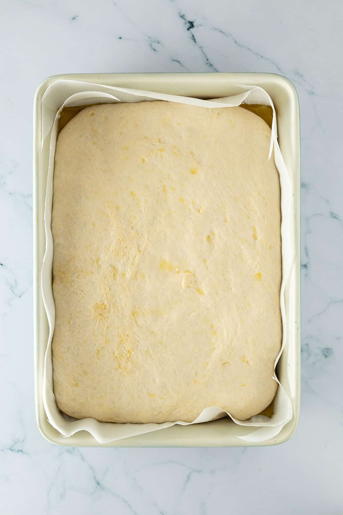 Aufgegangener Focaccia-Teig in einer mit Backpapier ausgelegten rechteckigen Backform.