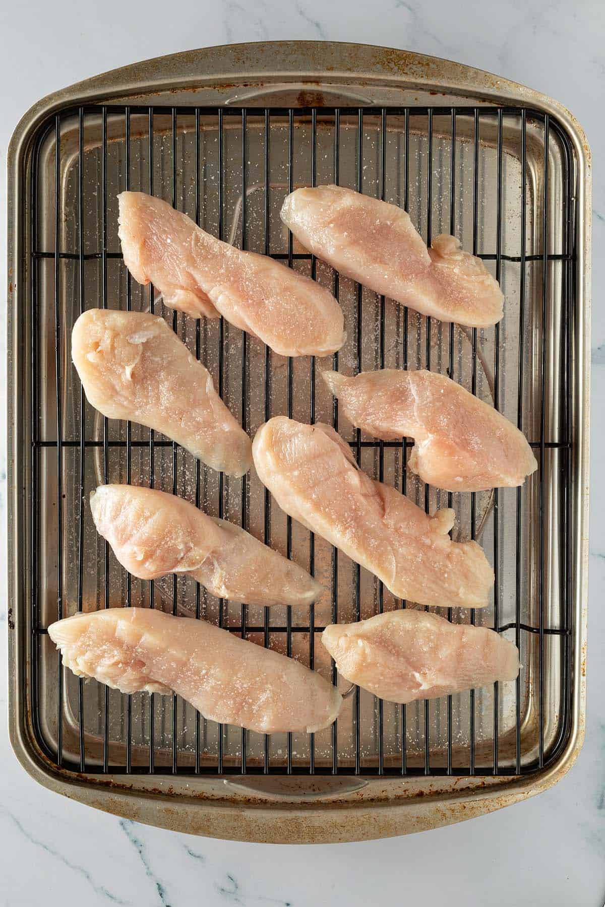 Gesalzene rohe Hähnchenstücke beim Dry Brining auf einem Gitter.
